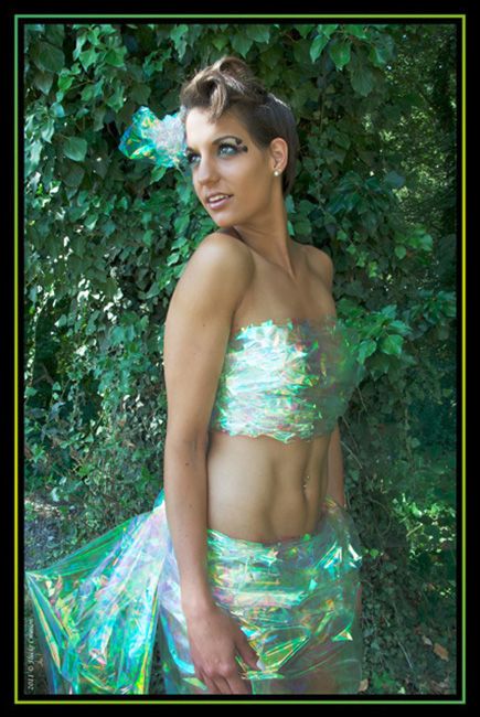 Modèle - Photographie d'un modèle féminin revêtue de cellophane brillant, posant devant mur de feuilles